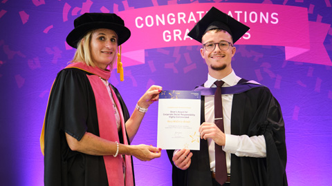 Two people in graduation attire; one hands a certificate to the other